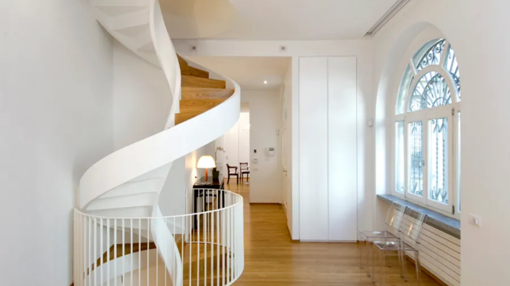 culptural white spiral staircase with wooden steps in a bright modern multi-story home interior.