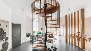 Contemporary wooden spiral staircase with black metal balusters in a bright, open-plan living space.