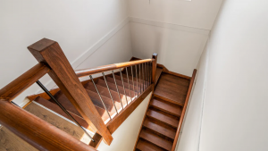 Wooden staircase with dark railing and slim metal balusters in a bright hallway.