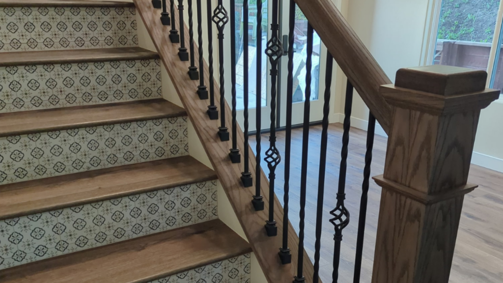 Close-up of a staircase renovation with patterned risers, wooden treads, and decorative wrought iron balusters.