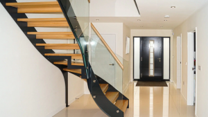 Modern open-concept staircase featuring wood treads, a black metal frame, and glass railings in a contemporary home entryway.