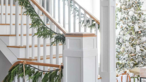 Holiday staircase decorating: White staircase decorated with lush green garland and golden ribbon for Christmas.