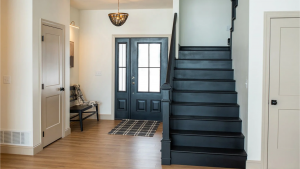 Black staircase with matching handrail in a modern entryway featuring wood floors, white walls, and black front doors.